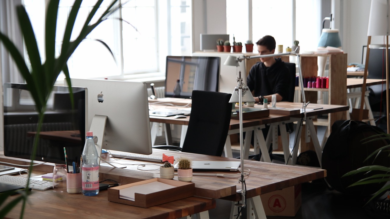 an office with multiple desks and a man looking at a computer.