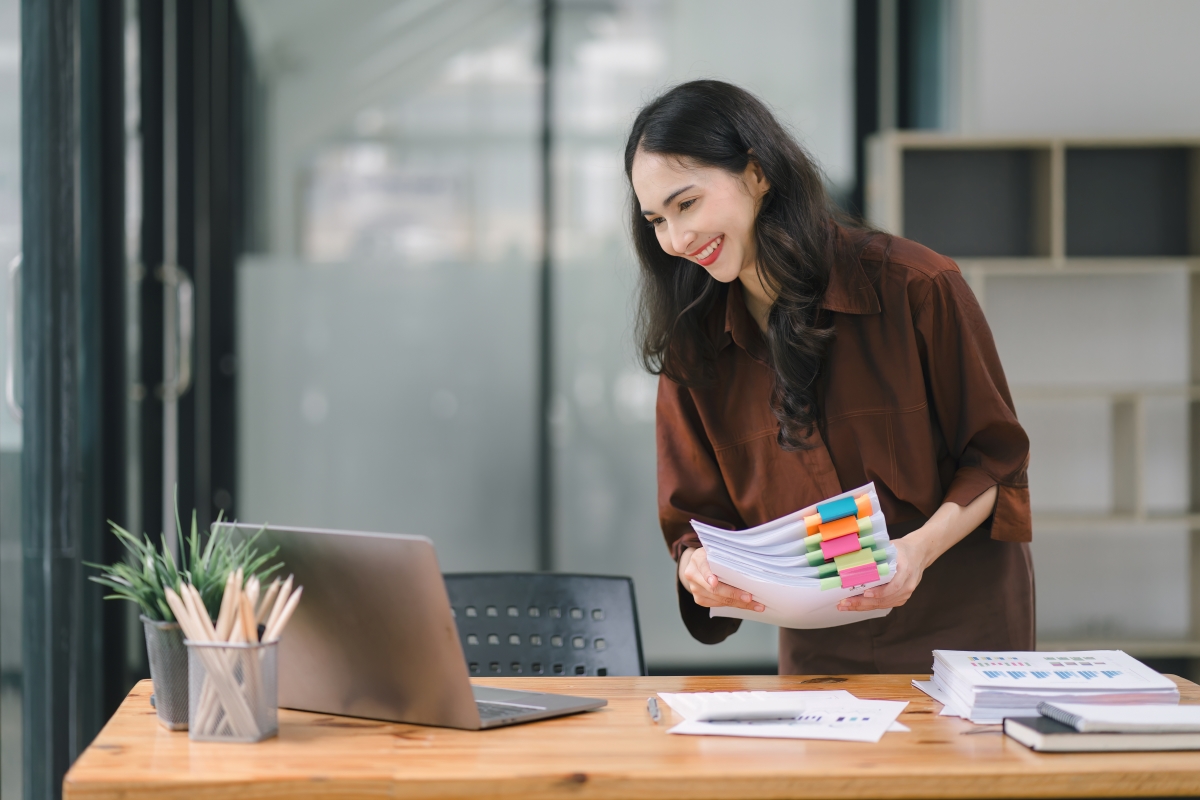 a person holding papers and looking at a laptop