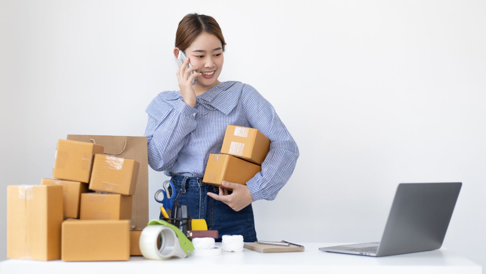 Business owner looking at laptop with products in boxes in her arm