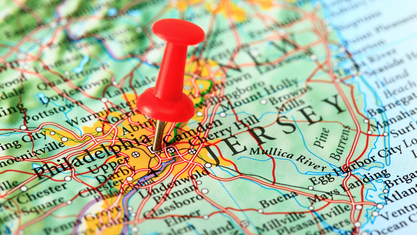 A red pushpin marks a location on a detailed map, highlighting the area between Philadelphia and New Jersey. The map features roads and city names.