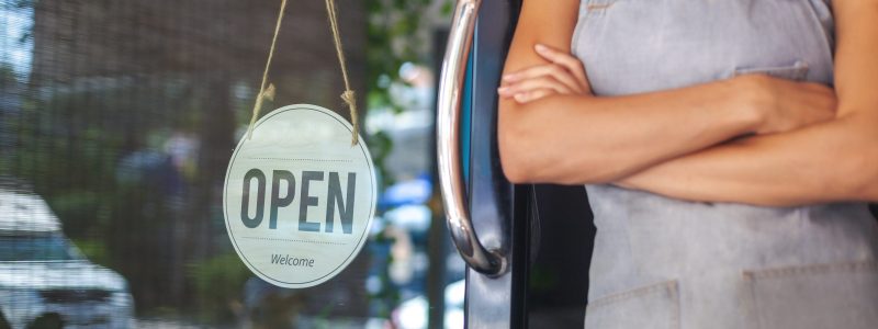 a small business owner standing next to an "open" sign