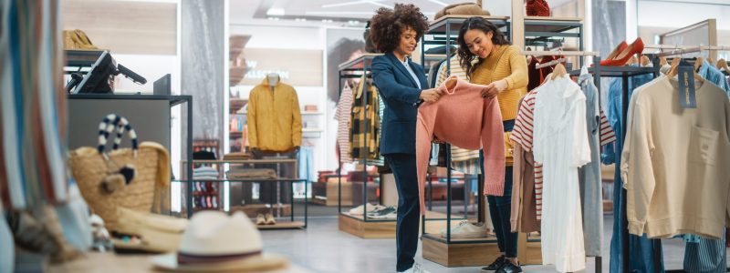 Customers Shopping in Modern Clothing Store, Retail Sales Associate Assists Client.